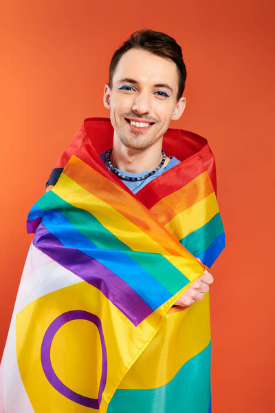 positive appealing young gay men in cozy attires with rainbow flag on orange backdrop, pride month