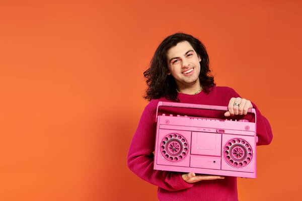 merry appealing gay man in magenta sweatshirt with long hair holding tape recorder smiling at camera