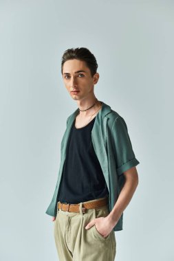 A young man proudly poses in a green shirt and tan pants, showcasing his vibrant queer fashion in a studio setting. clipart