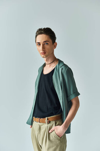 A young man proudly poses in a green shirt and tan pants, showcasing his vibrant queer fashion in a studio setting.
