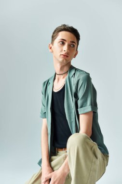Gri bir stüdyo stüdyosunun arka planında canlı yeşil bir gömlek ve taba rengi bir pantolon içinde poz veren tuhaf bir genç..