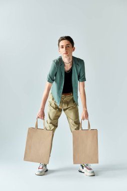 A young queer person holding two shopping bags against a gray background, expressing joy and pride in their purchases. clipart