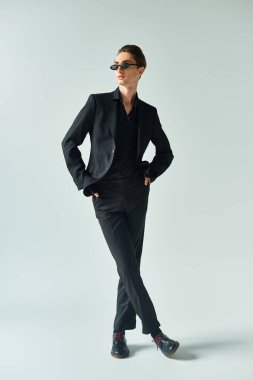 Young queer man in a stylish black suit striking a confident and proud pose against a grey background. clipart