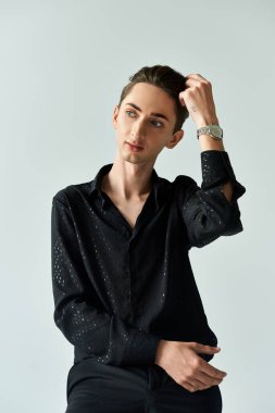 LGBTQ + topluluğunu gururla temsil eden genç bir adam, gri bir arka plana karşı bir stüdyoda güven içinde poz veriyor..