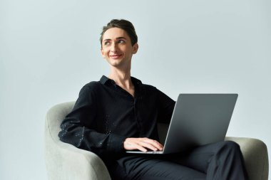 A young queer person on a grey background sits in a chair with a laptop, exuding confidence and pride in their digital presence. clipart