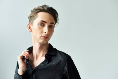 Siyah gömlekli genç bir adam stüdyoda gri bir arka plana karşı zarif bir poz veriyor ve LGBT topluluğuna gururunu gösteriyor..