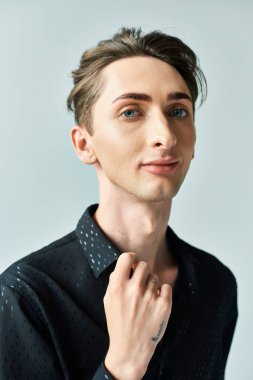 Siyah tişörtlü genç bir adam stüdyoda poz veriyor. Gri bir zemine karşı duruyor. Kendine güveni ve gururu var..