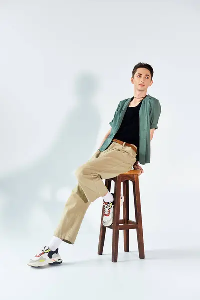 stock image A young queer person in a thoughtful pose while sitting on a stool against a white backdrop.