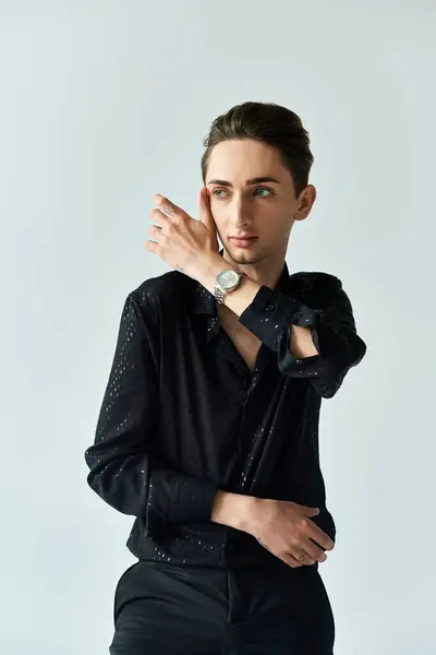 stock image A young man in a black shirt exudes confidence while posing in a studio setting against a grey background, embracing his LGBT identity.