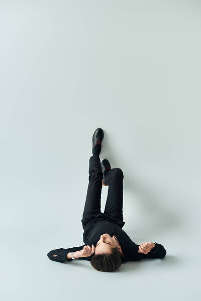 A young queer person peacefully lays on his back on a white background.