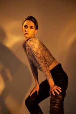 Deri pantolonlu genç bir ibne kameraya kendine güvenen bir poz verir. Cesur ve şık elbisesini gösterir..