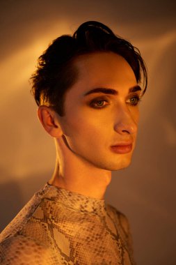 A young queer man in a snake skin dress stands gracefully in front of a bright light, exuding pride and style. clipart
