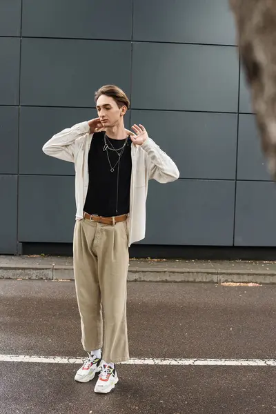 Stock image A young queer person in a stylish tan shirt and pants standing confidently on a city street.