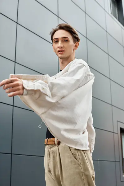 stock image A young queer person, stylishly dressed in a white shirt and tan pants, exudes confidence and pride in their attire.