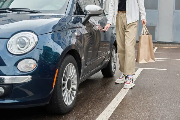 stock image A young queer person in stylish attire stands next to a blue car, exuding pride and confidence.