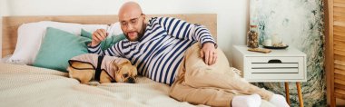 Handsome man with glasses peacefully lays beside his French bulldog on a cozy bed. clipart