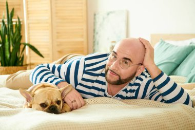 A man with glasses peacefully lying on a bed with his french bulldog. clipart