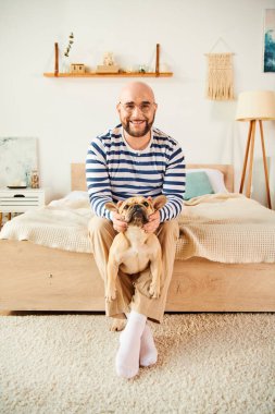Gözlüklü bir adam Fransız Bulldog 'unu tutarken yatakta dinleniyor..