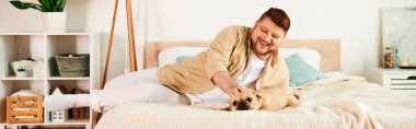 A man lounges alongside his French bulldog on a bed. clipart