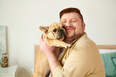 Yakışıklı adam evinde kucağında küçük bir Fransız Bulldog 'u tutuyor..