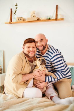 Erkek, evcil köpeğini kucağında tutarken yatakta sevgi ve şefkat gösteriyor..