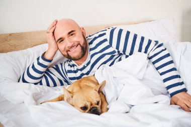 Bir adam, sevgili Fransız Bulldog 'uyla yatakta huzur içinde dinleniyor..