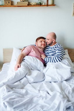 Two men relax on a bed at their home clipart