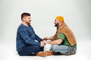 İki adam beyaz zeminde oturuyor ve bağ kuruyor..