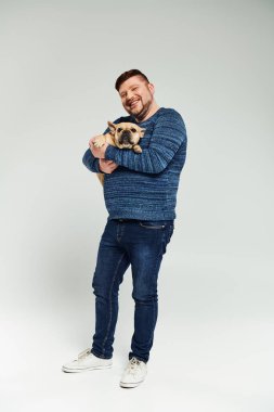 Bir adam nazikçe kucağında küçük bir Fransız bulldog tutuyor..