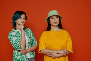 A striking scene featuring an Asian mother and her teenage daughter standing gracefully in front of a bold red wall. clipart