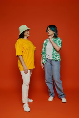 An Asian mother and her teenage daughter stand side by side in a studio against an orange background. clipart