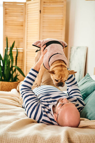 Handsome man in glasses relaxing on bed with his loyal french bulldog by his side.