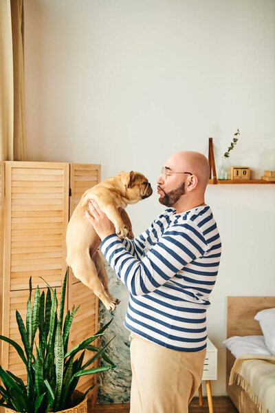 A man lovingly embraces a French bulldog against his face.