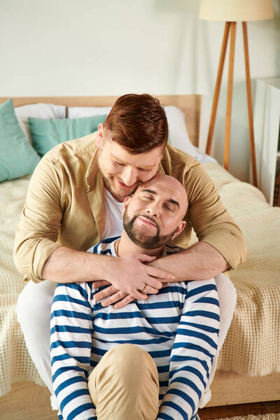 Two men hug on a bed at home in cozy attires.