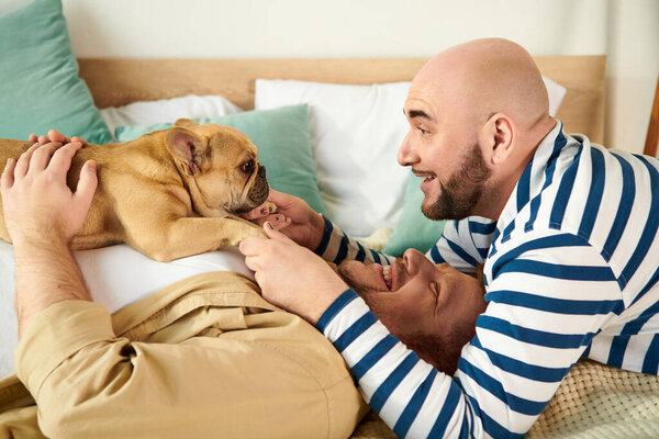 Two men relax in bed with their French Bulldog.