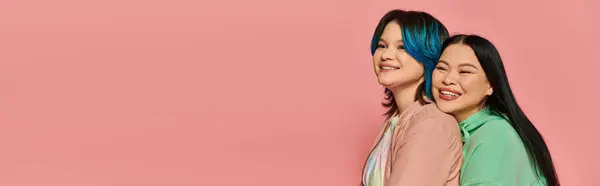 stock image Two women, an Asian mother and her teenage daughter, stand together in a studio wearing casual clothing on a pink background.