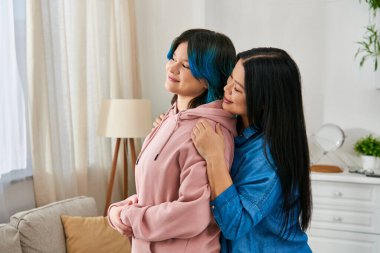 Asyalı bir anne ve genç kızı, rahat bir oturma odasında yan yana duruyorlar..