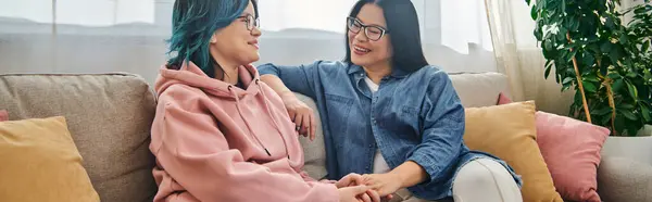 stock image An Asian mother and her teenage daughter in casual wear, sitting closely on top of a couch, sharing a tranquil moment together.