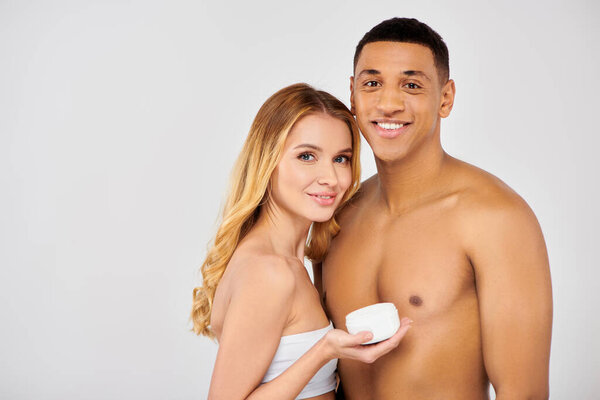 A stylish couple poses together, holding a cup of cream, showing their love for skincare.