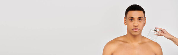 Hand of young woman with parfume near african american man.