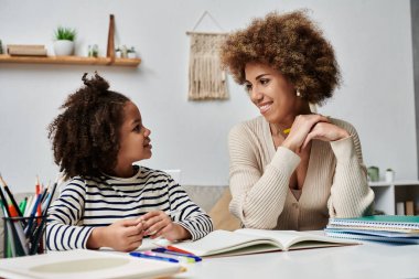 Afrika kökenli Amerikalı bir anne ve genç bir kız evlerinde öğrenme ve kaynaşma ile meşgul bir şekilde bir masada oturuyorlar..