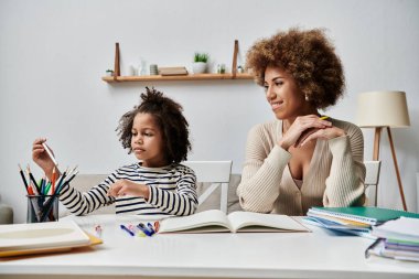 Mutlu bir Afro-Amerikan anne ve kızı bir masada oturmuş, evde kaliteli vakit geçiriyorlar..