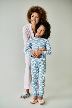 A cheerful African American mother and daughter strike a pose in matching pajamas against a grey backdrop. clipart