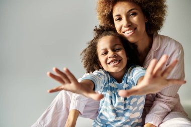 Pijamalı mutlu bir Afrikalı anne ve kız, gri bir arka planda kameraya poz veriyorlar..