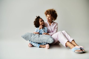 Afrika kökenli Amerikalı bir anne ve kız pijamalarıyla yerde oturup sıcak ve neşeli bir anı paylaşıyorlar..