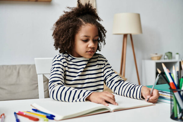 Молодая девушка афроамериканского происхождения сидит за столом, поглощенная записями в блокноте