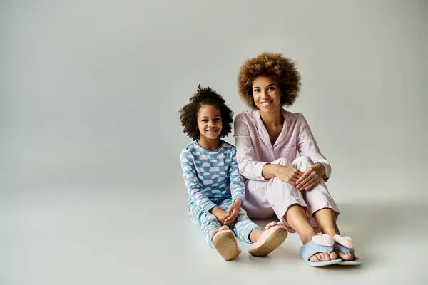 stock image An African American mother and daughter happily sitting on the floor in pajamas, enjoying a cozy moment together.