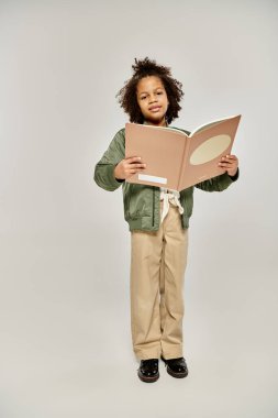 Elinde kitap olan genç bir kız, sayfalardan büyülenmiş, beyaz bir arkaplanın önünde duruyor..