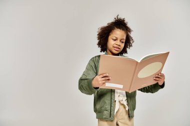 A little girl engrossed in reading a book on a white background. clipart