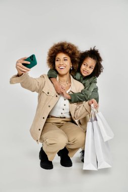 Kıvırcık Afrikalı Amerikalı anne ve kız şık kıyafetler içinde alışveriş torbalarıyla mutlu bir selfie çekiyorlar..